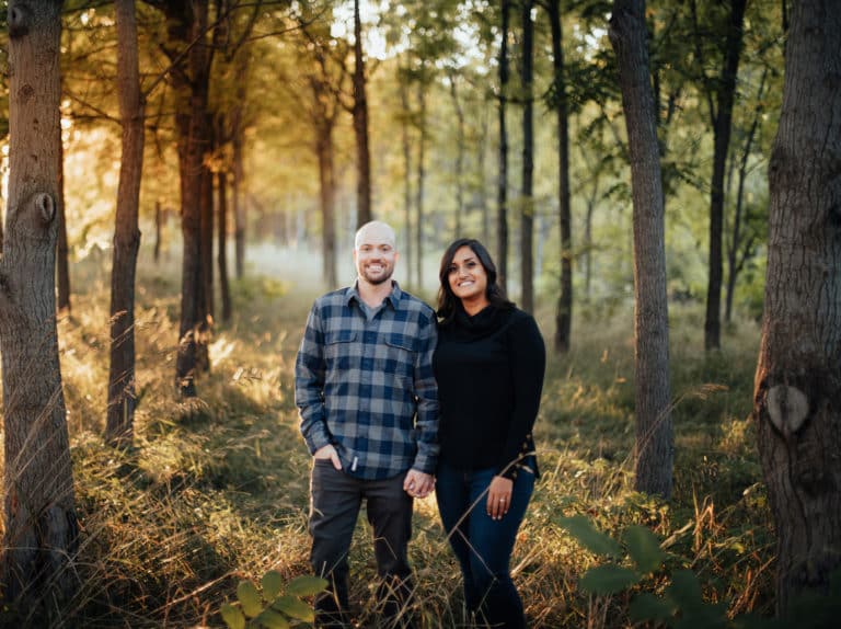 man with hands in his pocket is standing beside woman in forest