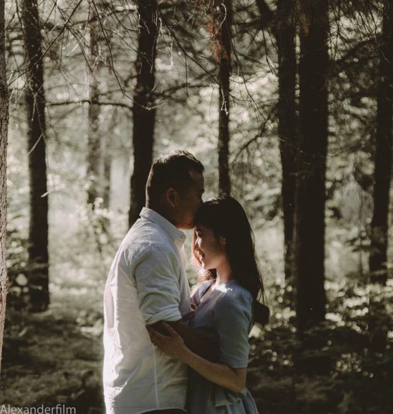 man kissing woman's for-head in the forest. sunshine is on covering her face