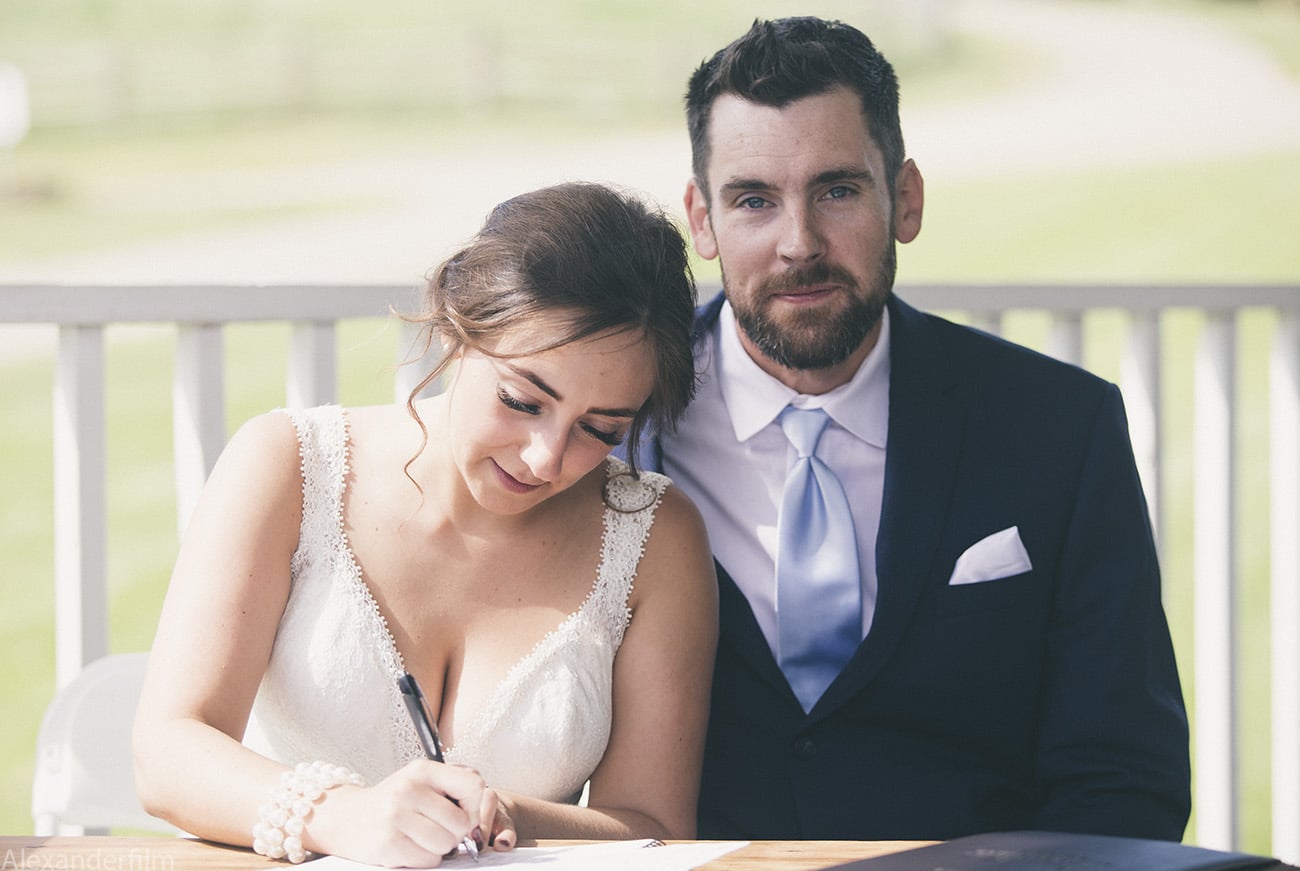 a bride signing papers as the man looks at the camera