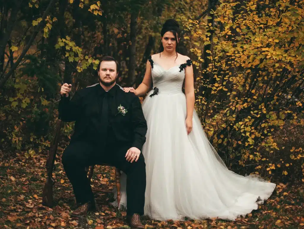 bride and groom in wedding outfits. groom sitting on a chair with gun