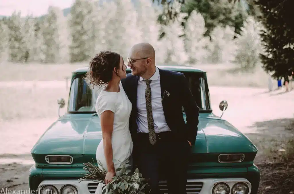 Newly married couple looking at each-other in front of a vintage truck