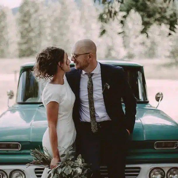 Newly married couple looking at each-other in front of a vintage truck