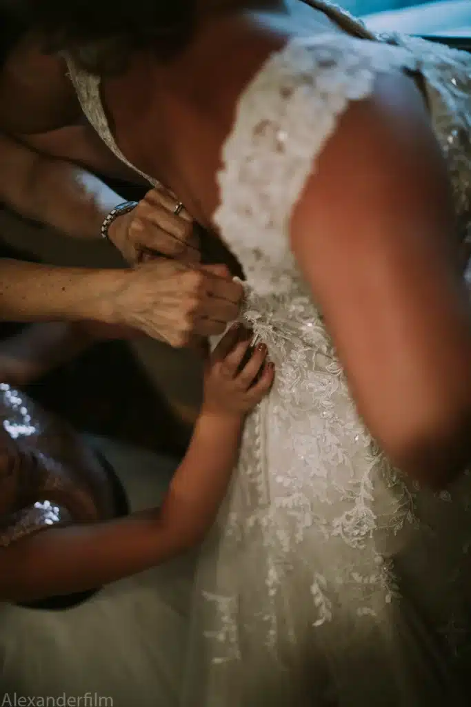 lots of hands helping button up wedding dress