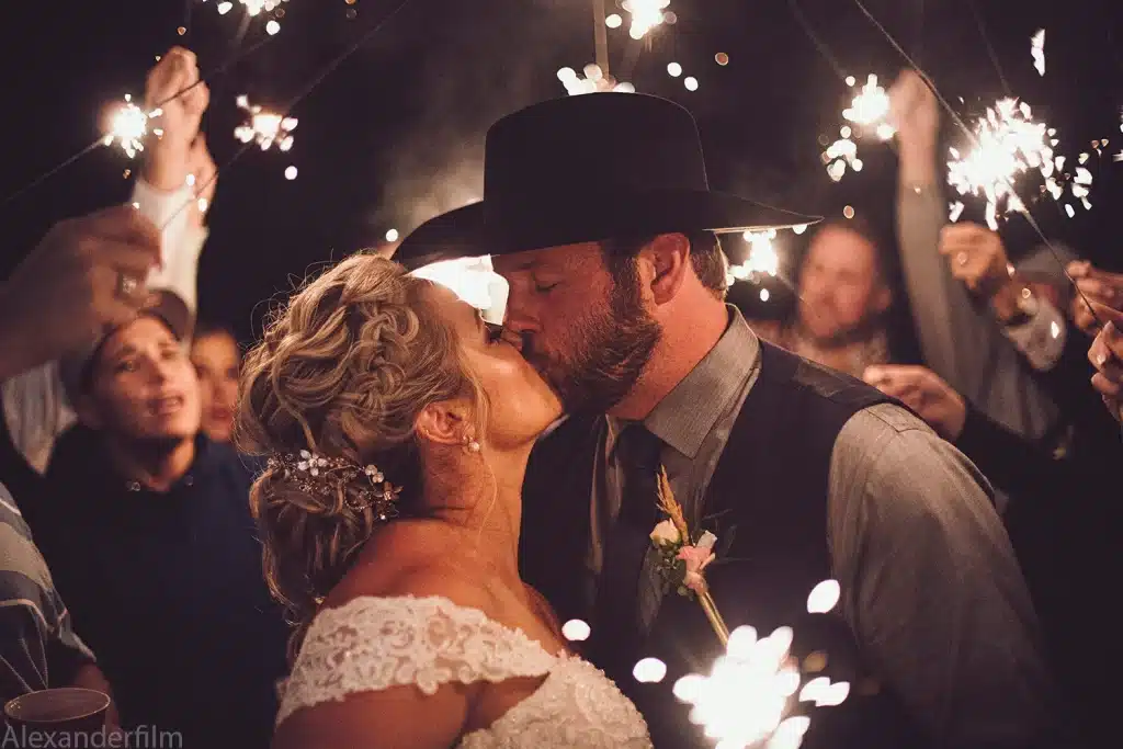 newly married couple kissing with guests behind them holding sparklers