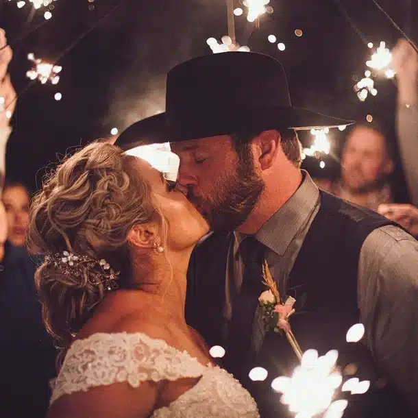 newly married couple kissing with guests behind them holding sparklers